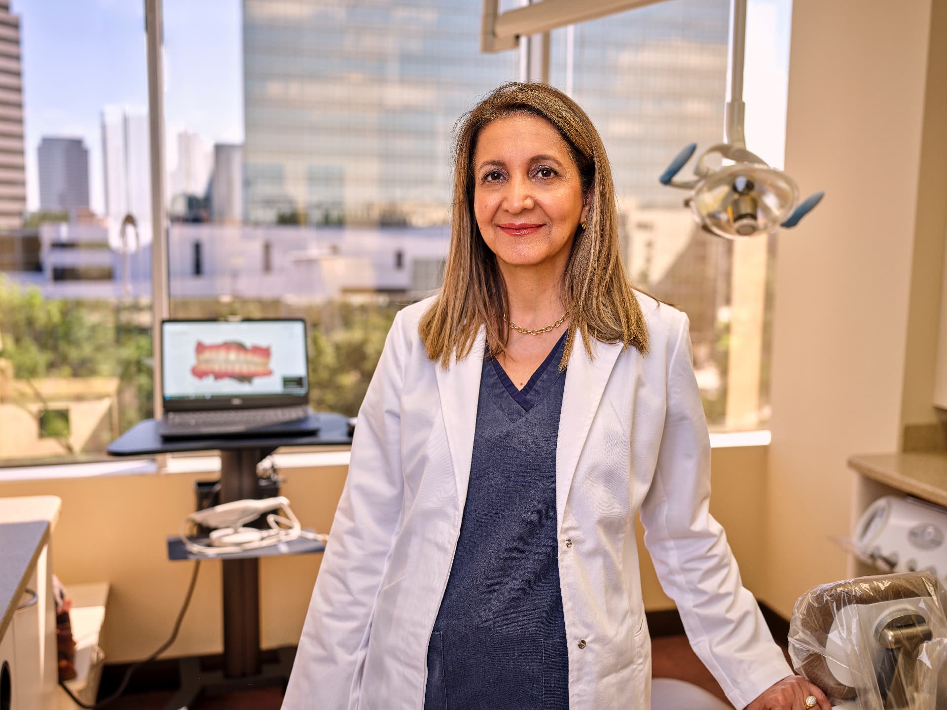 Dr. Nicki Tajalli standing in a treatment room at Uptown Dentistry with the Houston skyline behind her