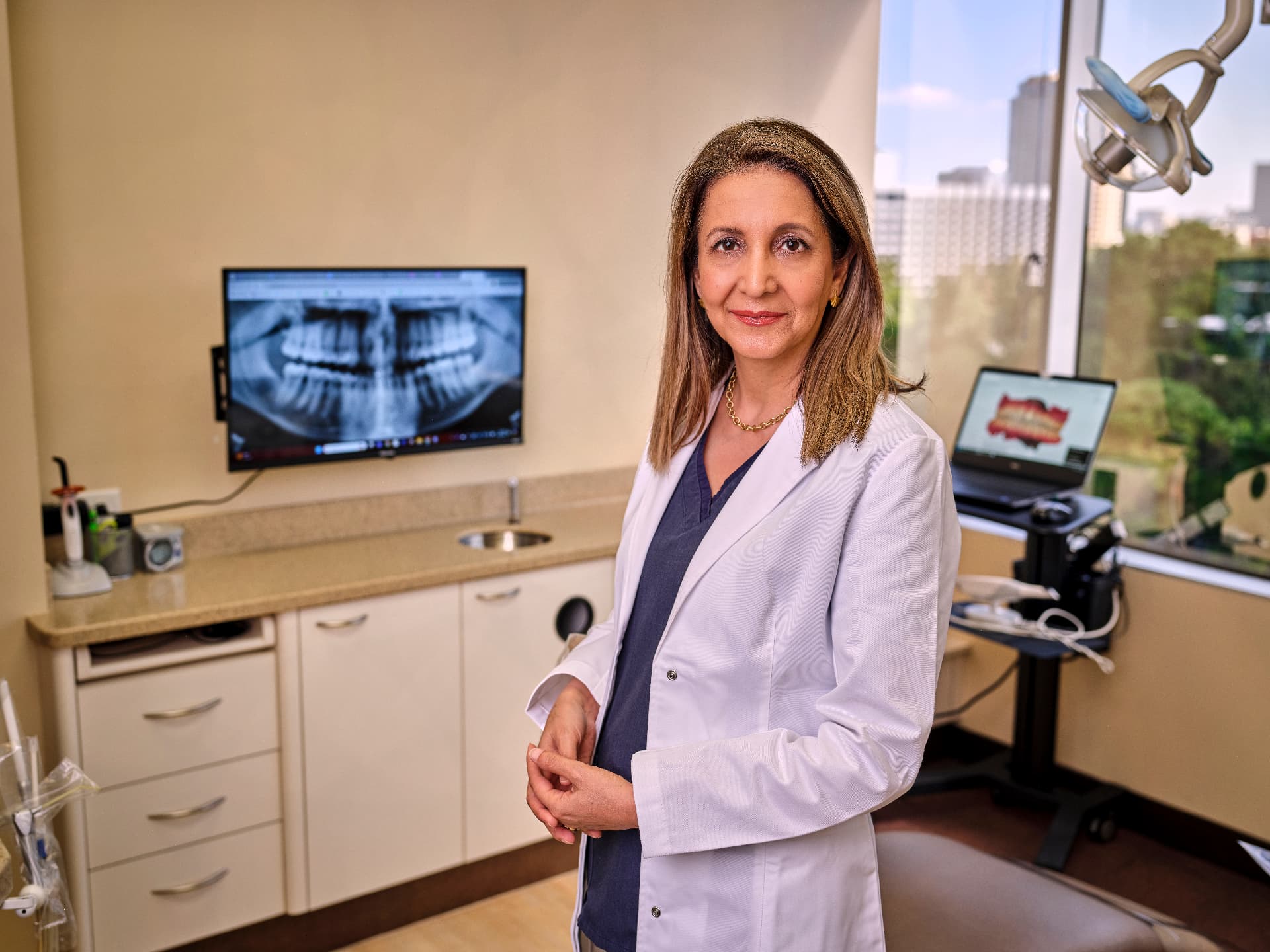 Dr. Nicki Tajalli beside a panoramic dental X-ray in her Uptown Houston treatment room
