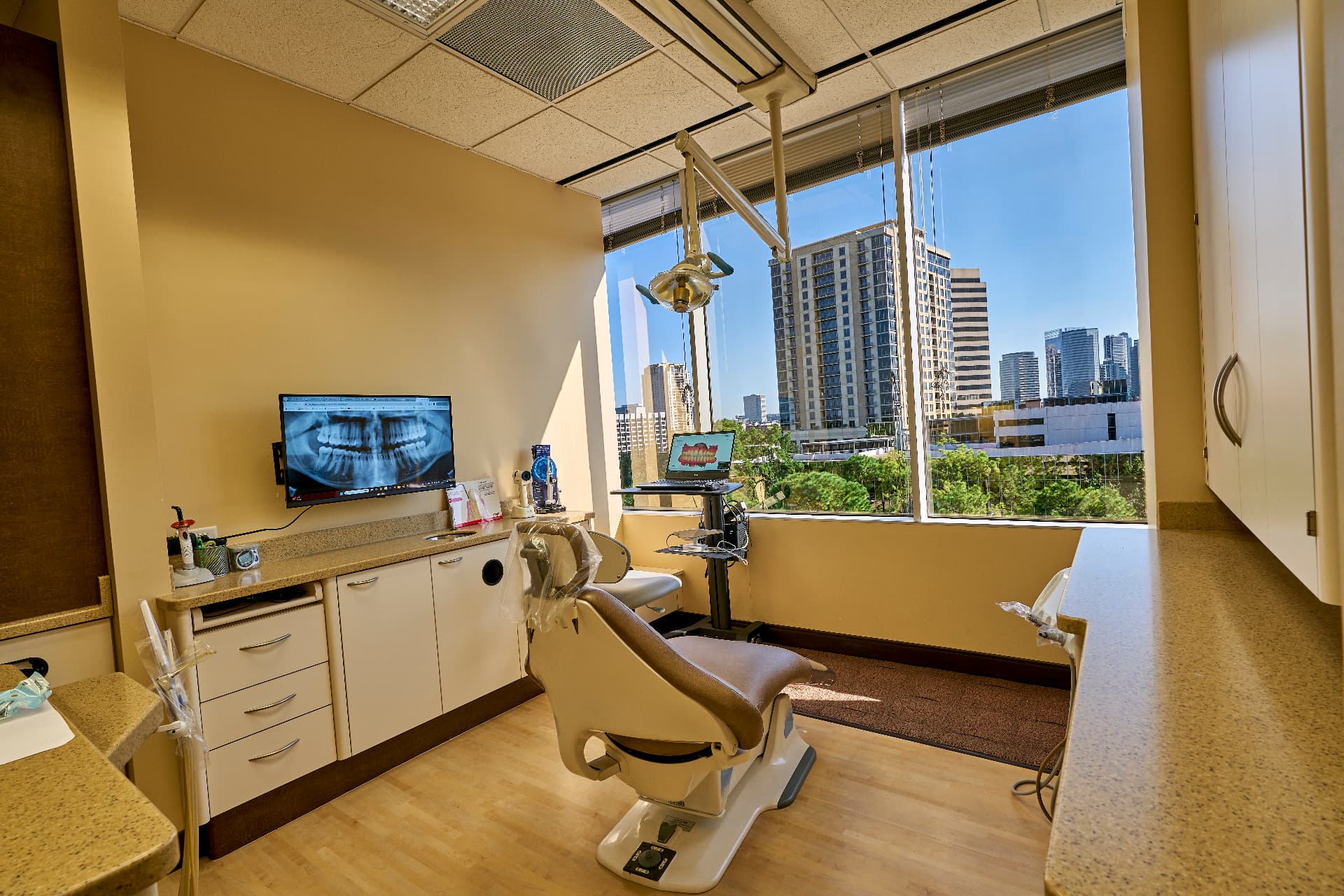 Treatment room at Uptown Dentistry with digital X-ray display and windows overlooking the Uptown Houston skyline